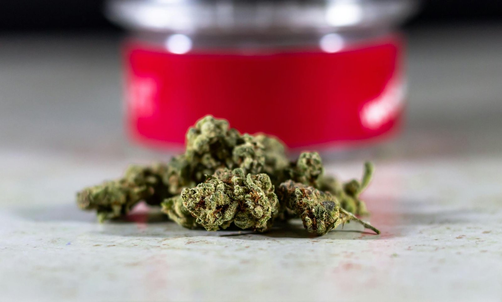 Close-up view of cannabis buds with a blurred container background on a table.