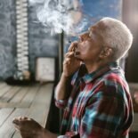 Elderly man enjoying a marijuana joint indoors, highlighting legal use.