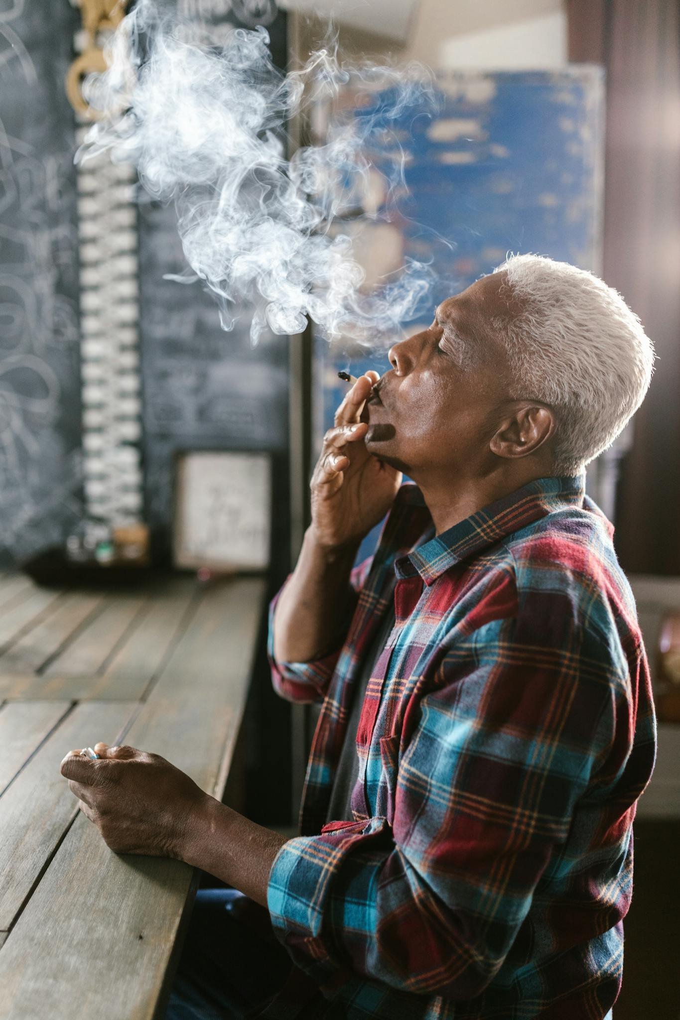 Elderly man enjoying a marijuana joint indoors, highlighting legal use.